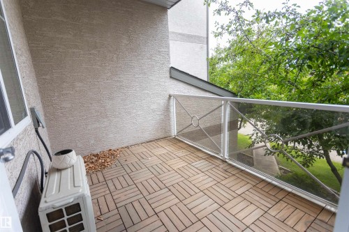 Private balcony with wood-finish tile flooring, stucco exterior walls, and a metal and glass railing - #204 2420 108 St Nw, Edmonton, AB - Outdoor With Exterior