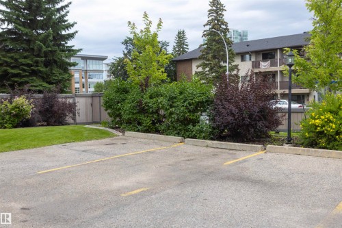 Paved parking area featuring designated spaces, concrete parking curbs, and surrounding established landscaping - #204 2420 108 St Nw, Edmonton, AB - Outdoor