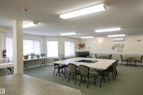 Spacious communal room with textured ceiling, multiple window units, wall-mounted air conditioning, and a built-in fireplace feature - #204 2420 108 St Nw, Edmonton, AB - Indoor Photo Showing Dining Room