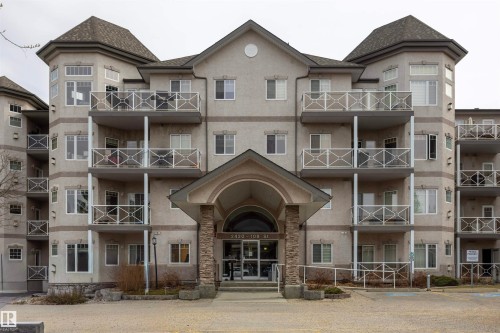 Multi-story condominium building featuring a stucco exterior, multiple private balconies with decorative railings, and a prominent arched entrance with stone column accents - #204 2420 108 St Nw, Edmonton, AB - Outdoor With Facade