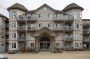 Multi-story condominium building featuring a stucco exterior, multiple private balconies with decorative railings, and a prominent arched entrance with stone column accents - #204 2420 108 St Nw, Edmonton, AB 