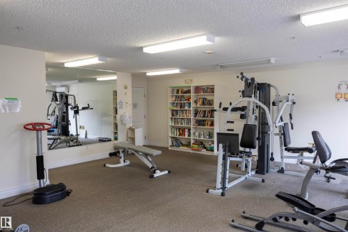Fitness room with wall-to-wall carpeting, overhead fluorescent lighting, and a mirrored wall - #204 2420 108 St Nw, Edmonton, AB - Indoor Photo Showing Gym Room