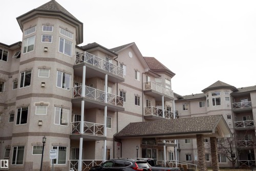 Multi-story residential building with a textured facade, several balconies featuring glass and metal railings, and a prominent turret-style architectural element - #204 2420 108 St Nw, Edmonton, AB - Outdoor With Facade
