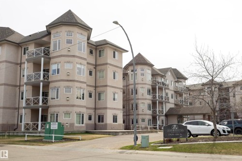 Multi-story building featuring turret-style architectural elements, private balconies with decorative railings, and a paved parking area - #204 2420 108 St Nw, Edmonton, AB - Outdoor With Facade