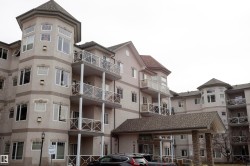 Multi-story residential building with a textured facade, several balconies featuring glass and metal railings, and a prominent turret-style architectural element - 