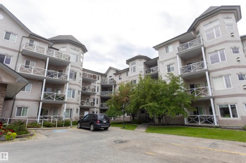 Multi-story stucco exterior with multiple private balconies featuring decorative railings, and a paved parking area - #204 2420 108 St Nw, Edmonton, AB - Outdoor With Facade