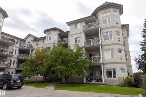 Multi-story residential building featuring multiple private balconies with decorative railings, bay windows, and a landscaped property with mature trees and green spaces - #204 2420 108 St Nw, Edmonton, AB - Outdoor With Facade