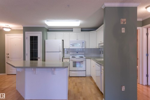Kitchen featuring white cabinetry, light-toned countertops, tile backsplash, and light wood-finish flooring - #204 2420 108 St Nw, Edmonton, AB - Indoor Photo Showing Kitchen