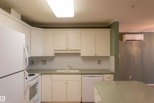 Cream cabinetry with gold-toned hardware, white subway tile backsplash, integrated sink, and white appliances - #204 2420 108 St Nw, Edmonton, AB - Indoor Photo Showing Kitchen
