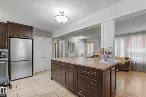 Kitchen featuring a central island with built-in storage, stainless steel refrigerator, tile flooring, and a decorative archway - 4323 114B Street Nw, Edmonton, AB - Indoor Photo Showing Kitchen