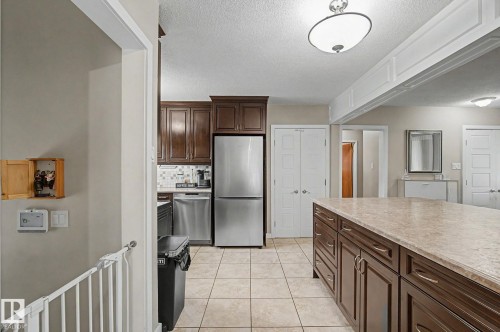 Kitchen featuring stainless steel appliances, dark wood cabinetry, a tiled backsplash, and a large central island with a light-colored countertop - 4323 114B Street Nw, Edmonton, AB - Indoor Photo Showing Kitchen