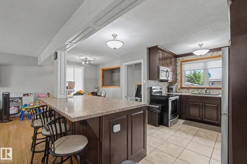 Kitchen featuring dark wood-finish cabinetry, stainless steel appliances, tile backsplash, and an island with countertop seating - 4323 114B Street Nw, Edmonton, AB - Indoor Photo Showing Kitchen