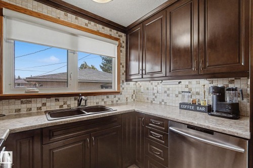 Dark wood cabinetry, mosaic tile backsplash, double basin sink with stainless steel faucet, light-toned countertops, and a stainless steel dishwasher - 4323 114B Street Nw, Edmonton, AB - Indoor Photo Showing Kitchen With Double Sink
