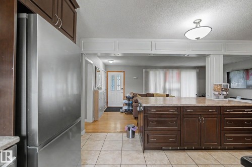 Stainless steel refrigerator, wood-finish cabinetry, tile flooring, and a large island with a stone-finish countertop - 4323 114B Street Nw, Edmonton, AB - Indoor Photo Showing Kitchen