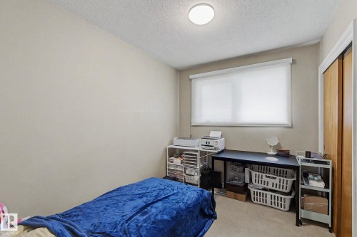 Neutral wall paint, ceiling-mounted light fixture, window with roller shade, carpeted flooring, and a built-in closet with wood-finish sliding doors - 4323 114B Street Nw, Edmonton, AB - Indoor Photo Showing Bedroom