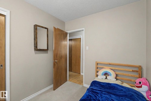 Carpeted flooring with painted walls, a wood-finish door, and a built-in closet with sliding wood-finish doors - 4323 114B Street Nw, Edmonton, AB - Indoor Photo Showing Bedroom