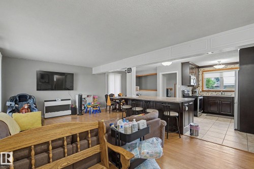 Open-concept living area featuring wood-finish flooring, a kitchen island with seating, dark wood cabinetry, a tiled kitchen floor, and a window with natural light - 4323 114B Street Nw, Edmonton, AB - Indoor