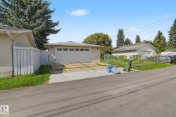 Detached garage with a paneled door, concrete driveway, and a white privacy fence - 