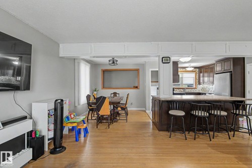 Hardwood-finish flooring, kitchen with dark wood cabinetry, integrated stainless steel refrigerator, and a kitchen island with seating - 4323 114B Street Nw, Edmonton, AB - Indoor
