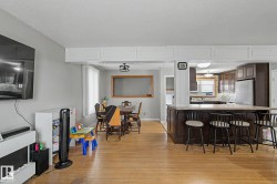Hardwood-finish flooring, kitchen with dark wood cabinetry, integrated stainless steel refrigerator, and a kitchen island with seating - 