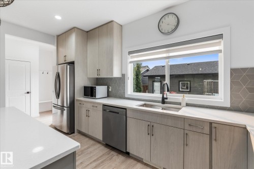 Contemporary kitchen featuring light wood-finish cabinetry, stainless steel appliances, a geometric tile backsplash, and a large window above the sink - 9 Dillingham Avenue, Fort Saskatchewan, AB - Indoor Photo Showing Kitchen With Double Sink