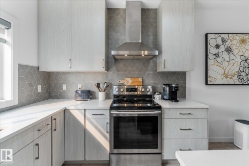 Modern kitchen featuring light wood-finish cabinetry, stainless steel range with matching range hood, geometric tile backsplash, and light-toned countertops - 9 Dillingham Avenue, Fort Saskatchewan, AB - Indoor Photo Showing Kitchen With Upgraded Kitchen