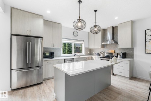 Kitchen featuring an island with a light-toned countertop, stainless steel appliances, wood-finish flooring, and pendant lighting - 9 Dillingham Avenue, Fort Saskatchewan, AB - Indoor Photo Showing Kitchen With Stainless Steel Kitchen With Upgraded Kitchen