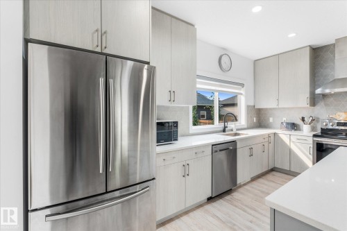 Light wood-finish cabinetry, stainless steel appliances, white countertops, geometric tile backsplash, and light wood-finish flooring - 9 Dillingham Avenue, Fort Saskatchewan, AB - Indoor Photo Showing Kitchen With Stainless Steel Kitchen With Upgraded Kitchen