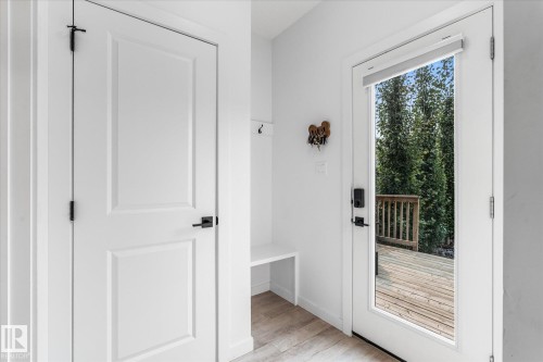 White paneled doors with matte black hardware, built-in bench, wood-finish flooring, and a full-light exterior door leading to a wood deck - 9 Dillingham Avenue, Fort Saskatchewan, AB - Indoor Photo Showing Other Room