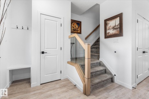 Wood-finish flooring, built-in bench with coat hooks, white panel doors, and a staircase with a glass and wood railing - 9 Dillingham Avenue, Fort Saskatchewan, AB - Indoor Photo Showing Other Room