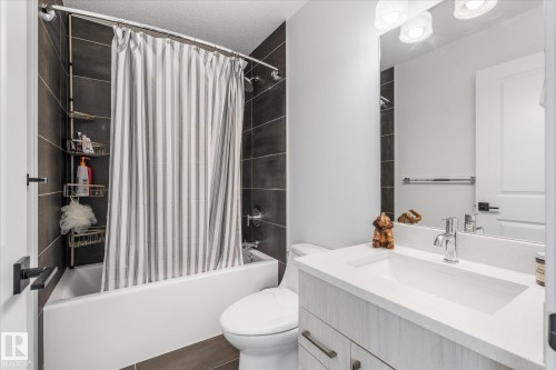 Bathroom featuring a tub/shower combination with dark tile surround, a built-in vanity with a single basin sink, and a wall-mounted mirror - 9 Dillingham Avenue, Fort Saskatchewan, AB - Indoor Photo Showing Bathroom