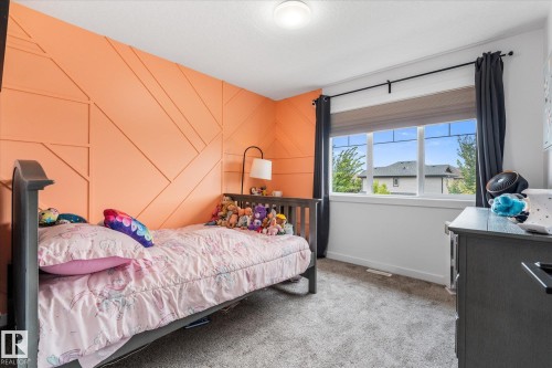 Accent wall with geometric paneling, carpeted flooring, large window with roller shade, ceiling-mounted light fixture, window with exterior scenery - 9 Dillingham Avenue, Fort Saskatchewan, AB - Indoor Photo Showing Bedroom