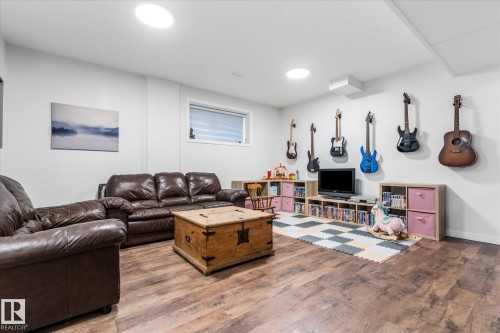Finished basement recreation room featuring wood-finish flooring, recessed ceiling lighting, and built-in shelving with pink cabinetry - 9 Dillingham Avenue, Fort Saskatchewan, AB - Indoor Photo Showing Living Room