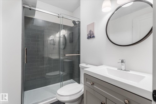 Glass-enclosed shower with subway tile, vanity with integrated sink, and a circular wall mirror - 9 Dillingham Avenue, Fort Saskatchewan, AB - Indoor Photo Showing Bathroom