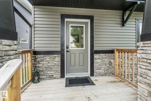 Front entry featuring a light gray door with window insert, wood-finish porch flooring, and stone veneer accents - 9 Dillingham Avenue, Fort Saskatchewan, AB - Outdoor With Exterior