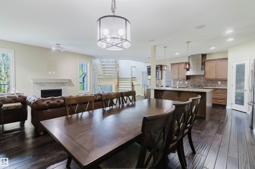 Open concept layout featuring wood-finish flooring, a kitchen with an island and pendant lighting, a fireplace with a stone surround, and a visible staircase - 864 Armitage Wynd Sw, Edmonton, AB - Indoor Photo Showing Dining Room With Fireplace