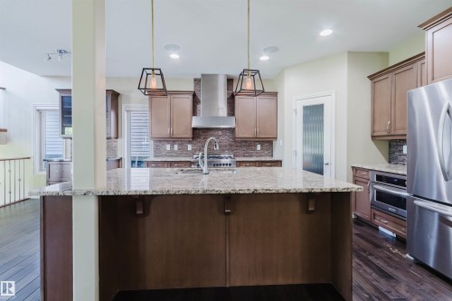 Kitchen featuring a large island with stone countertop, stainless steel appliances, pendant lighting, and wood-finish flooring - 864 Armitage Wynd Sw, Edmonton, AB - Indoor Photo Showing Kitchen With Upgraded Kitchen