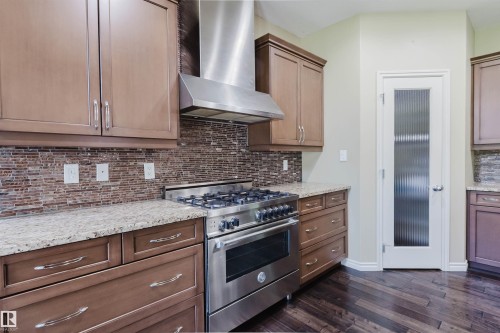 Stainless steel gas range with coordinating range hood, brown wood-finish cabinetry, granite countertops, and a full-height tile backsplash - 864 Armitage Wynd Sw, Edmonton, AB - Indoor Photo Showing Kitchen With Upgraded Kitchen