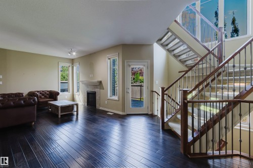 Expansive living area featuring rich wood-finish flooring, a built-in fireplace with a stone surround, and multiple windows - 864 Armitage Wynd Sw, Edmonton, AB - Indoor