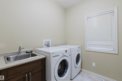 Utility room featuring a built-in sink with a countertop, dark wood-finish cabinetry, and a window with blinds - 864 Armitage Wynd Sw, Edmonton, AB - Indoor Photo Showing Laundry Room