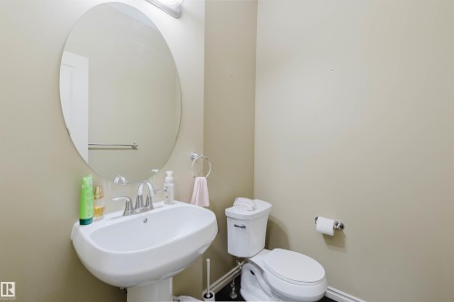 Pedestal sink with chrome faucet, oval wall mirror, and flush toilet - 864 Armitage Wynd Sw, Edmonton, AB - Indoor Photo Showing Bathroom