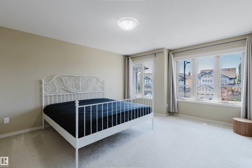 Neutral painted walls, light-colored carpeting, large windows with curtain rods, and a ceiling-mounted light fixture - 864 Armitage Wynd Sw, Edmonton, AB - Indoor Photo Showing Bedroom