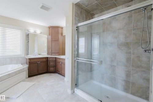 Dual vanity with wood-finish cabinetry, built-in soaking tub, tiled flooring, and a glass-enclosed shower with tiled walls - 864 Armitage Wynd Sw, Edmonton, AB - Indoor Photo Showing Bathroom