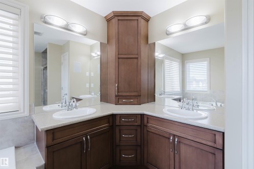 Dual vanity with undermount sinks and chrome fixtures, ample counter space, rich wood-finish cabinetry, and integrated storage tower - 864 Armitage Wynd Sw, Edmonton, AB - Indoor Photo Showing Bathroom
