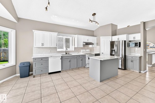 Kitchen featuring a central island, stainless steel appliances, two-tone cabinetry, tiled flooring, and vaulted ceilings - 16227 64 Street Nw, Edmonton, AB - Indoor Photo Showing Kitchen