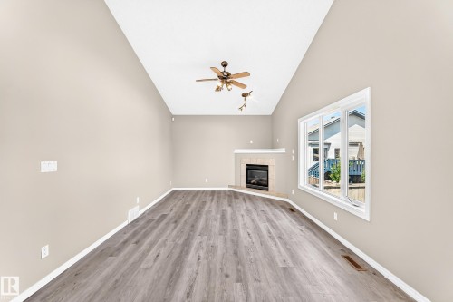 Vaulted ceiling, wood-finish flooring, corner fireplace with tile surround and mantel, and large window - 16227 64 Street Nw, Edmonton, AB - Indoor With Fireplace