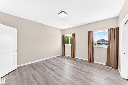 Light wood-finish flooring, two large windows, white trim, neutral wall tones, and overhead flush-mount lighting - 16227 64 Street Nw, Edmonton, AB - Indoor Photo Showing Other Room