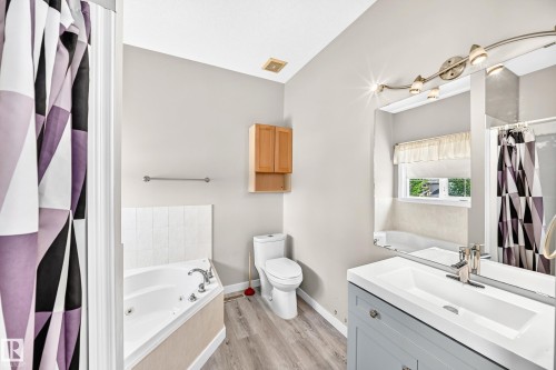 Bathroom featuring a corner jetted tub, a vanity with an integrated sink, and wood-finish flooring - 16227 64 Street Nw, Edmonton, AB - Indoor Photo Showing Bathroom