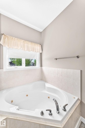 Corner jetted tub featuring polished chrome fixtures, tile surround, and a clear glass window - 16227 64 Street Nw, Edmonton, AB - Indoor Photo Showing Bathroom