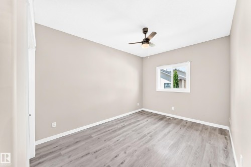 Neutral painted walls, wood-finish flooring, white trim, ceiling fan light fixture, and a window with white casing - 16227 64 Street Nw, Edmonton, AB - Indoor Photo Showing Other Room